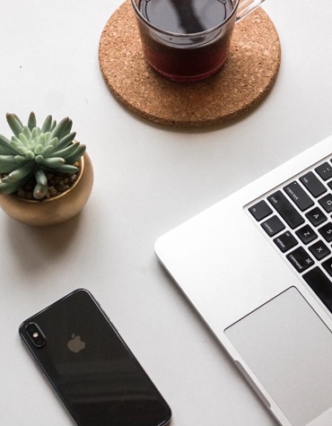 Overlooking a desk with a laptop keyboard, iPhone, succulent, and a cup of coffee.